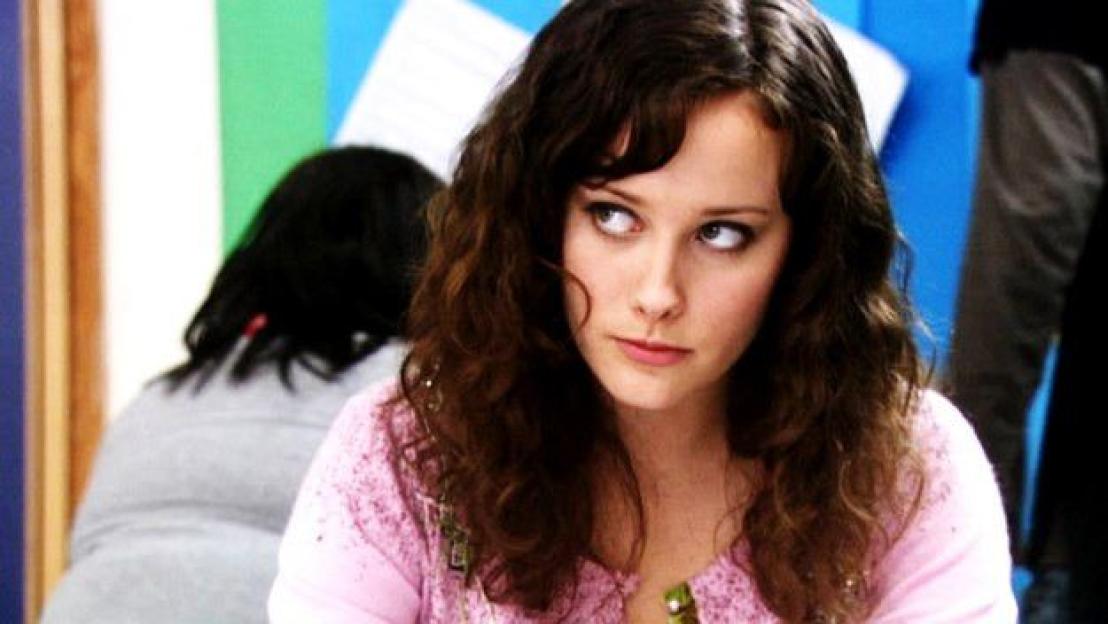 Michelle, a young woman with dark wavy hair, looking to the side with a serious expression.