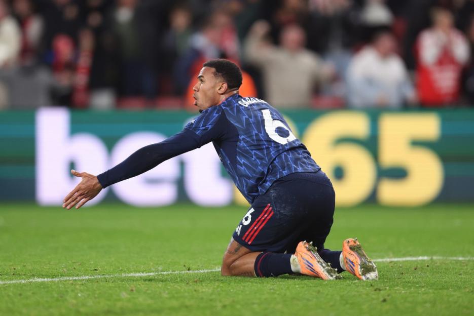A soccer player wearing a navy blue jersey with number 6 on his back, kneeling on the grass with arms outstretched.