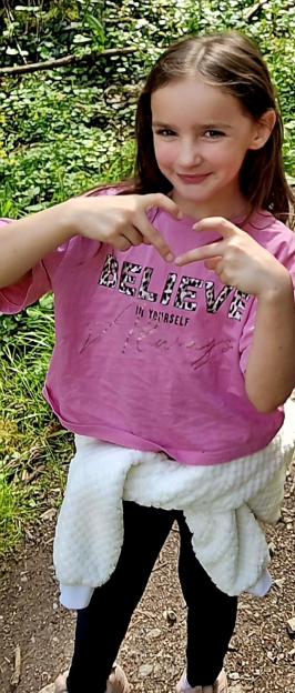 Aria Thorpe wearing a pink "Believe In Yourself" t-shirt and forming a heart with her hands.