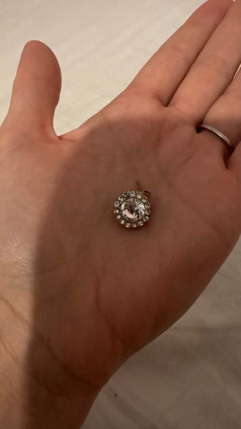A person's hand holding a single round diamond earring.