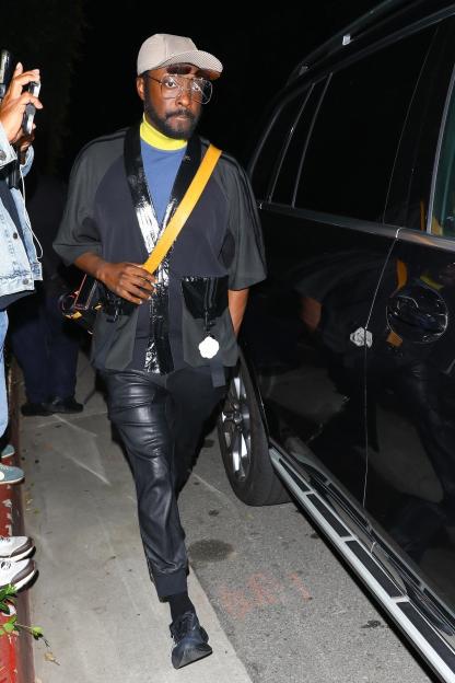 Will.i.am walking beside a black car.