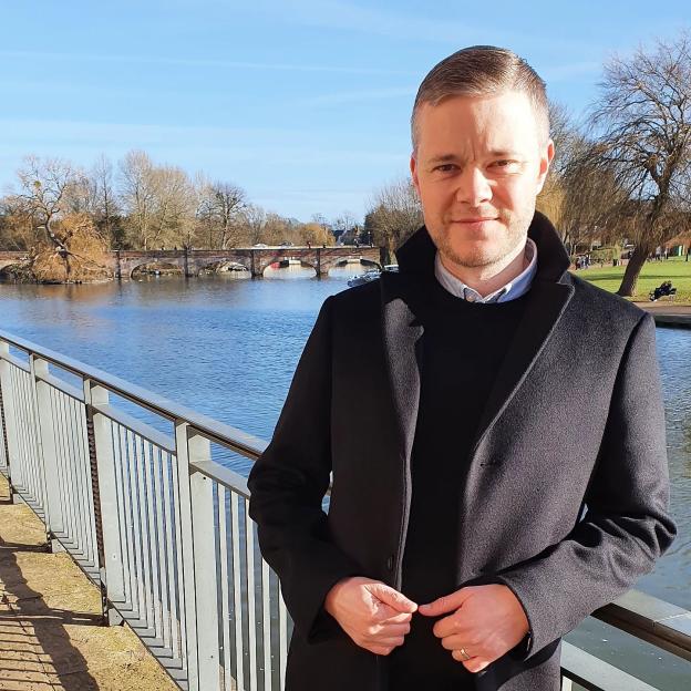 Mark Goldbridge from Utd Stand by a river with a bridge in the background.