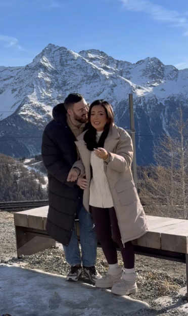 A smiling couple embracing in front of snowy mountains.