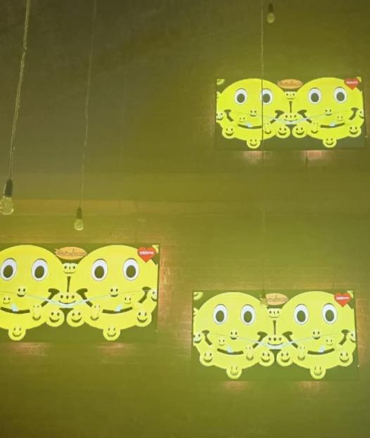 Two men at a bar with bright yellow, cartoonish faces displayed on screens above them.