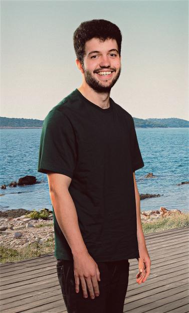 A smiling man, believed to be a cast member of "Virgin Island," stands on a wooden boardwalk by the sea.