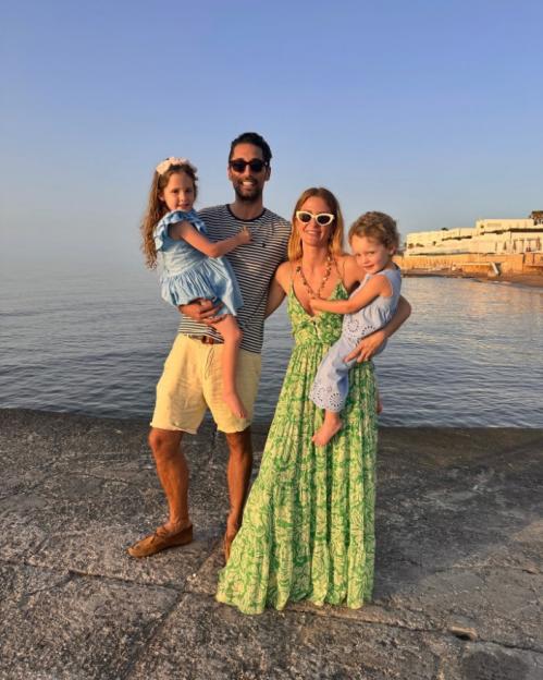 A man and woman each holding a young child standing by the ocean.