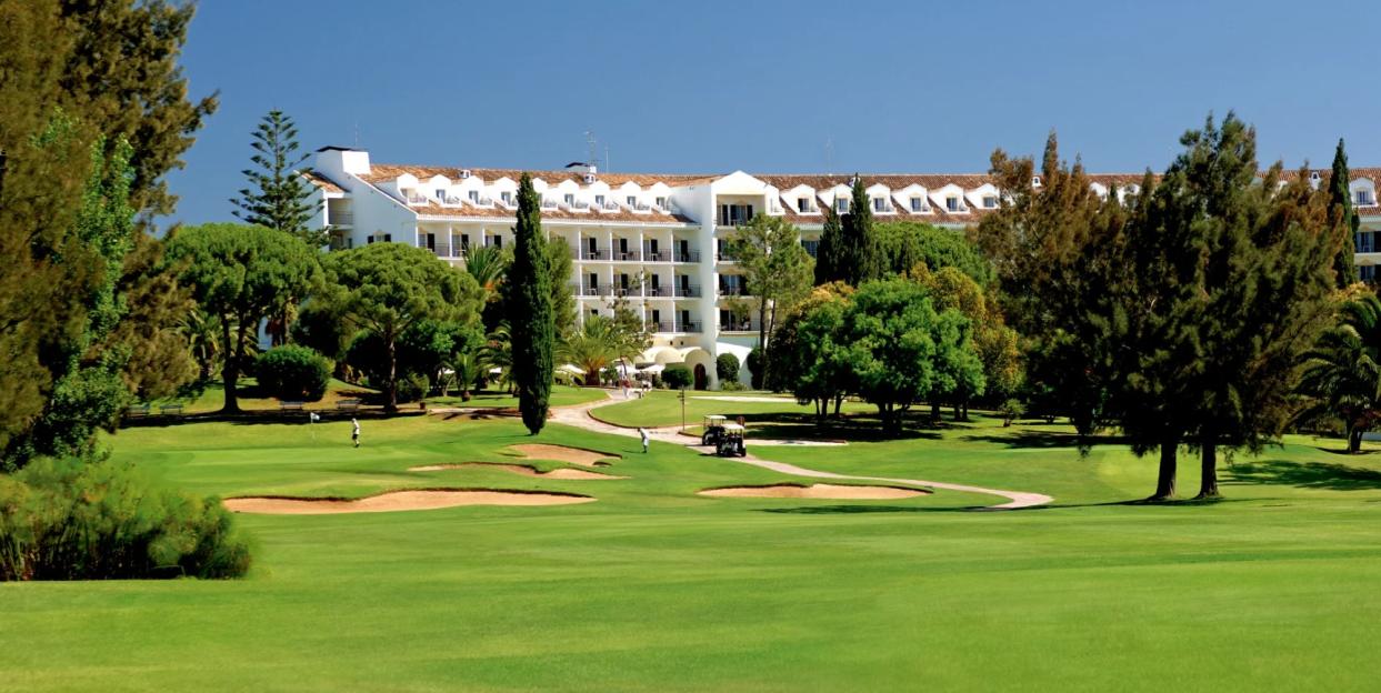 Penina Golf Resort with a large white hotel in the background, surrounded by green trees and golf course with sand traps and golfers.
