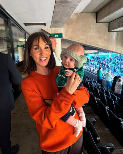 Megan McKenna holding her son Landon, who is wearing noise-canceling headphones, at a football stadium.