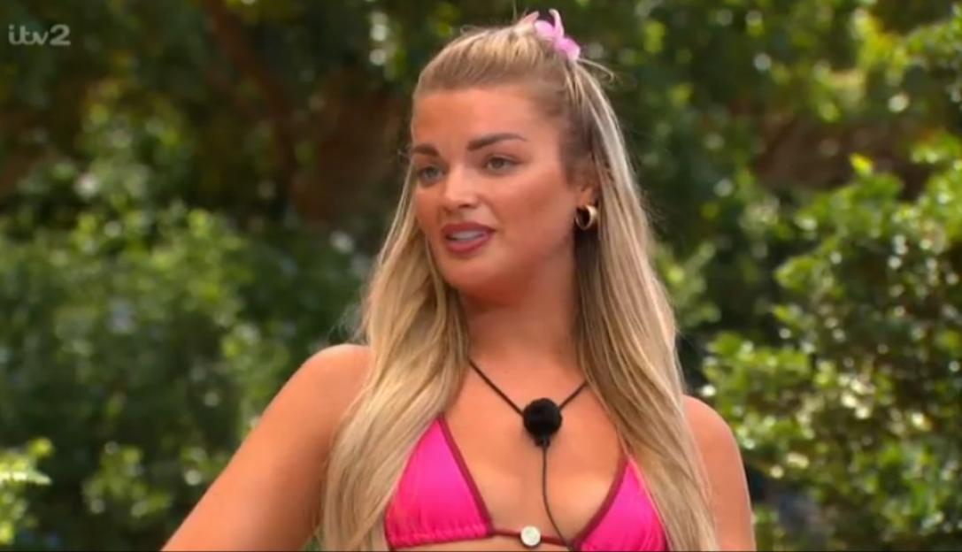 A young woman with blonde hair, wearing a pink bikini and a small pink hair clip, looking slightly to the right with her mouth open.