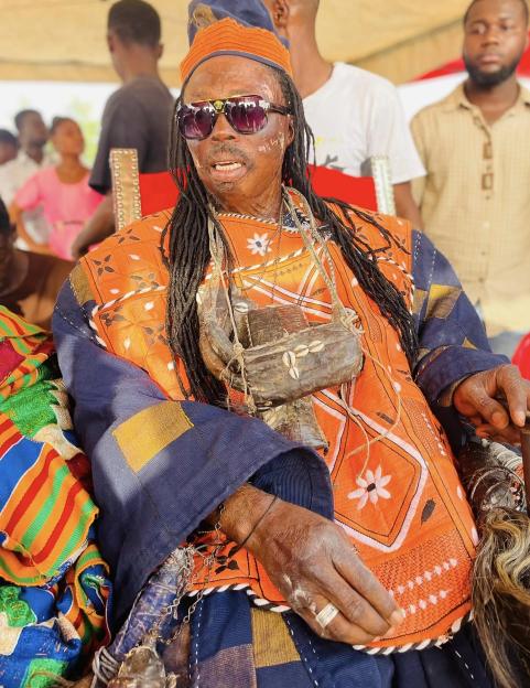 Nana Kwaku Bonsam, a witch doctor, seated in traditional attire and sunglasses.