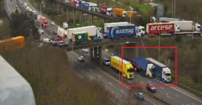 Overhead view of a highway with heavy traffic, with an overturned truck partially blocking a lane and causing a traffic jam.
