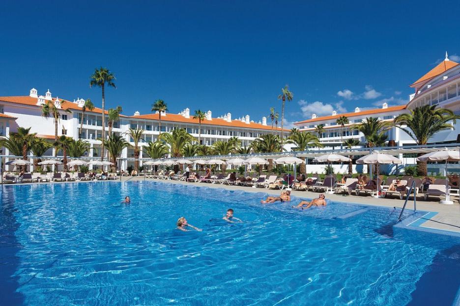 People swimming and lounging by the pool at Hotel Riu Arecas in Tenerife.
