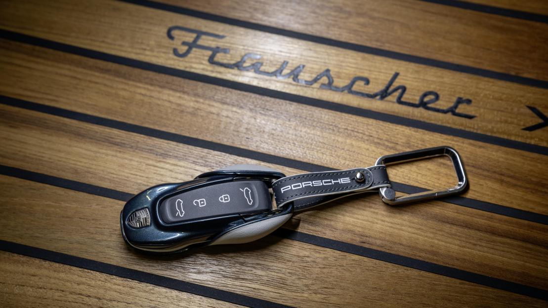 A dark blue Porsche car key with a black leather keychain on a wooden surface.