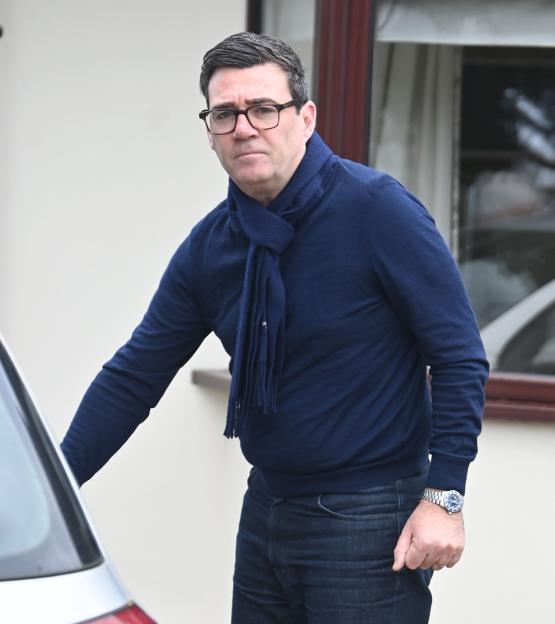Andy Burnham, dressed in a navy sweater, scarf, and jeans, looking towards the viewer.