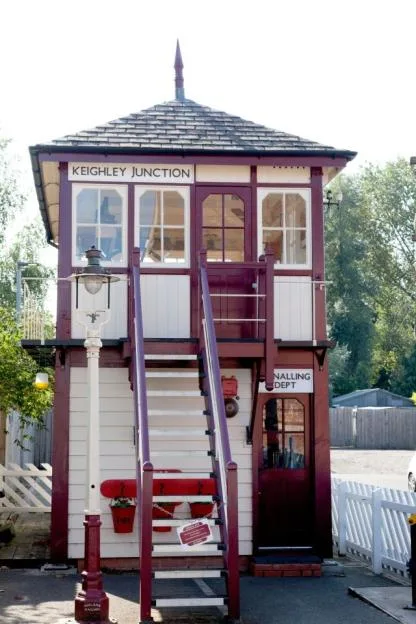 The Keighley Junction signal box, a two-story wooden structure painted cream and maroon with an external staircase leading to the upper floor.