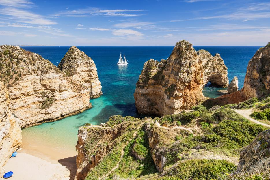 Beautiful beach on the Algarve coast, Portugal, with rock formations, a sailboat, and turquoise water.
