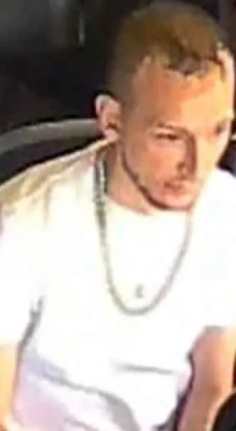 Surveillance photo of a young man with light brown hair wearing a white t-shirt and a silver chain necklace.