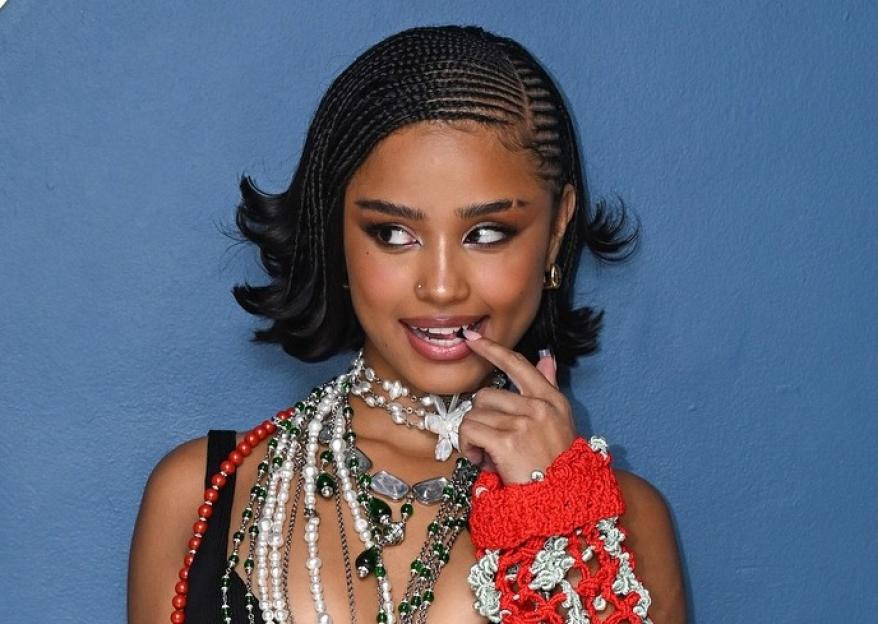 Tyla posing in a red crocheted outfit with many necklaces on the set of The Tonight Show Starring Jimmy Fallon.