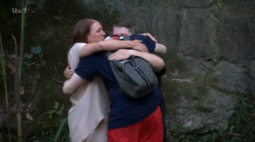 Woman in beige dress hugging two people.