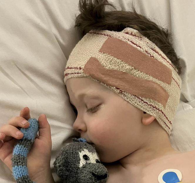 Raffi Starkowitz post-surgery in hospital with bandages on his head, holding a knitted toy.