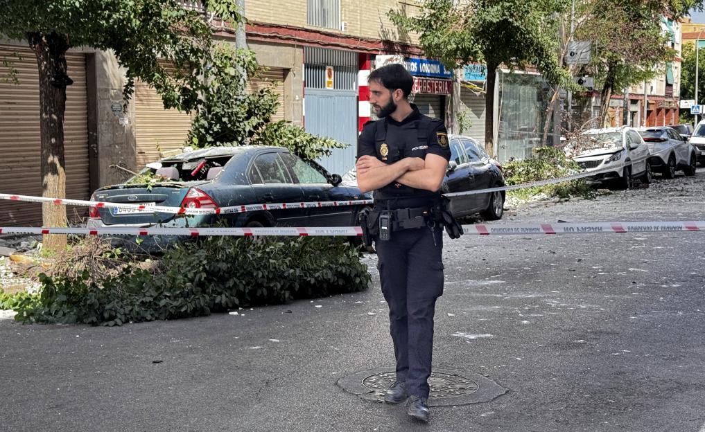 A police officer standing next to damaged cars and fallen debris after an earthquake in Spain.