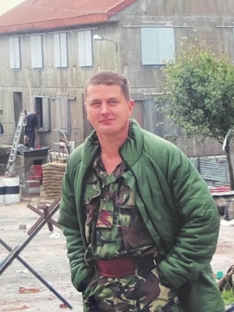 Paul Ainscough, a retired army sergeant major, stands outdoors in military fatigues and a green puffer jacket.