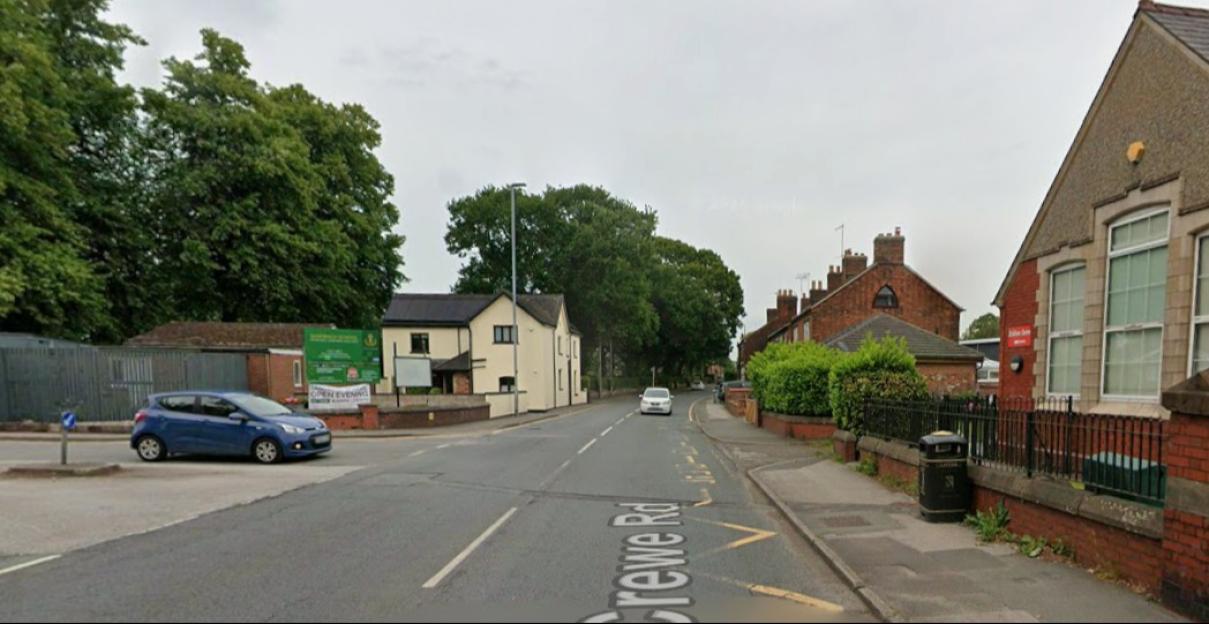 A road named "Crewe Rd" with a blue car parked on the left, a white car driving in the distance, and brick buildings lining both sides of the street.
