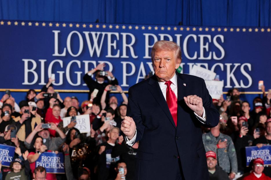 U.S. President Donald Trump gestures with clenched fists in front of a blue banner that reads "LOWER PRICES BIGGER PAYCHECKS" while speaking to a crowd.