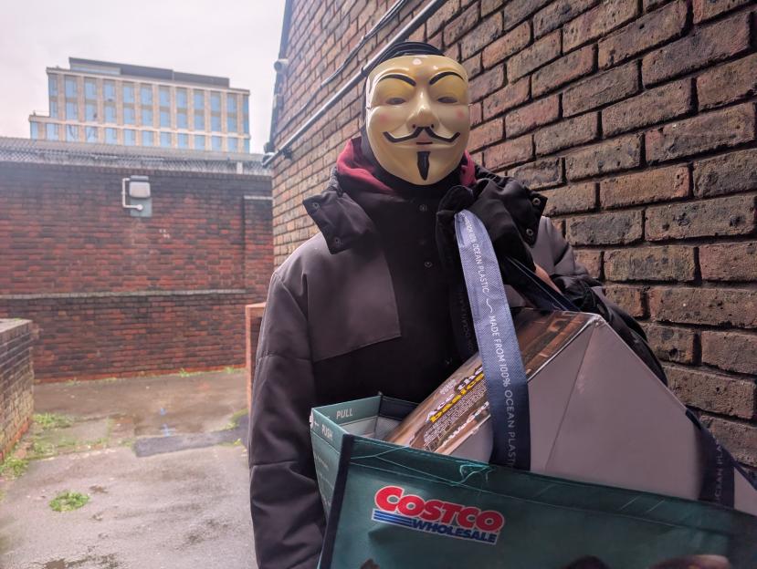 A masked parcel thief carrying a parcel in an alleyway.