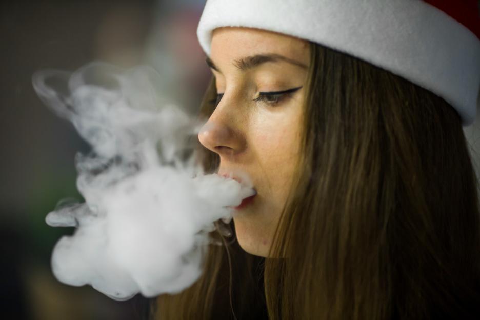 Closeup of a woman holding and smoking an electronic cigarette, with vapor exhaling from her mouth.