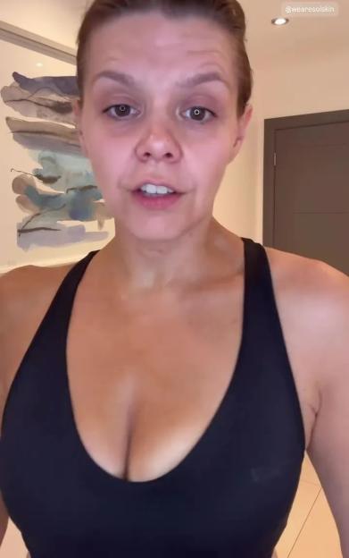 A woman in a black sports bra, with hair pulled back, looks directly at the camera.