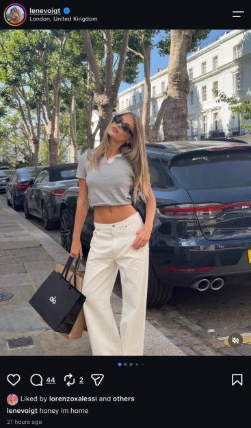 A woman in white pants and a striped crop top holds shopping bags on a London street.