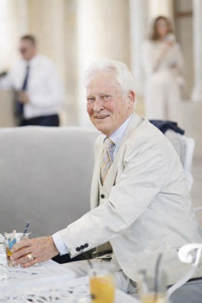 Dave Bootle, former Sun features leader, in a cream suit, smiling and holding a drink.