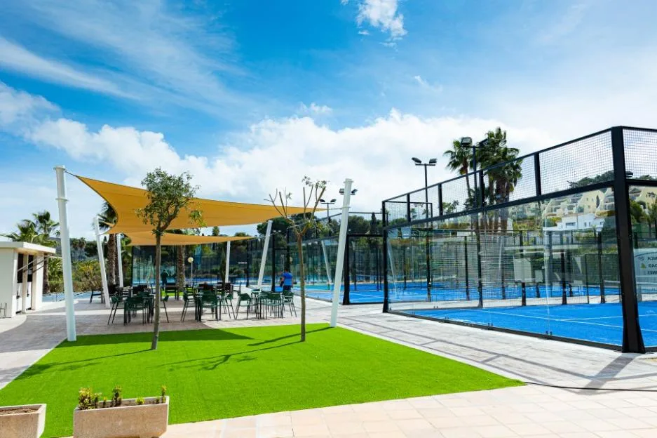 Outdoor padel tennis courts and a shaded seating area at La Manga Club under a partly cloudy sky.