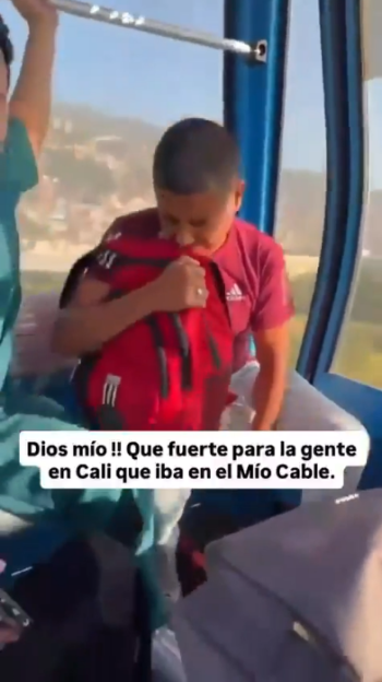 A young boy in a cable car, holding his red backpack to his mouth, seemingly distressed or crying, with another person visible to his left, during an earthquake.