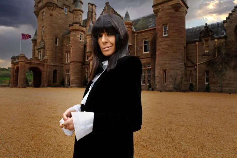Presenter Claudia Winkleman standing in front of a Scottish castle.