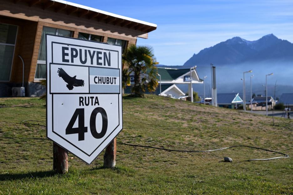 A street sign for Epuyen, Chubut and Ruta 40, with mountains and buildings in the background.
