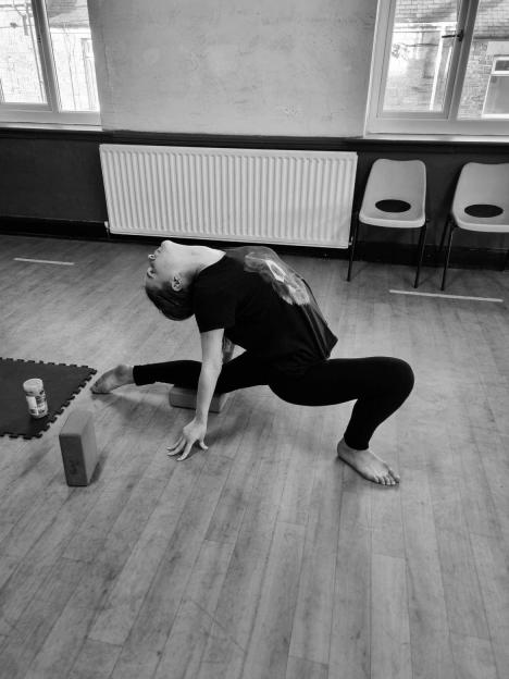 A black and white photo of Holly Newton stretching in a dance studio.