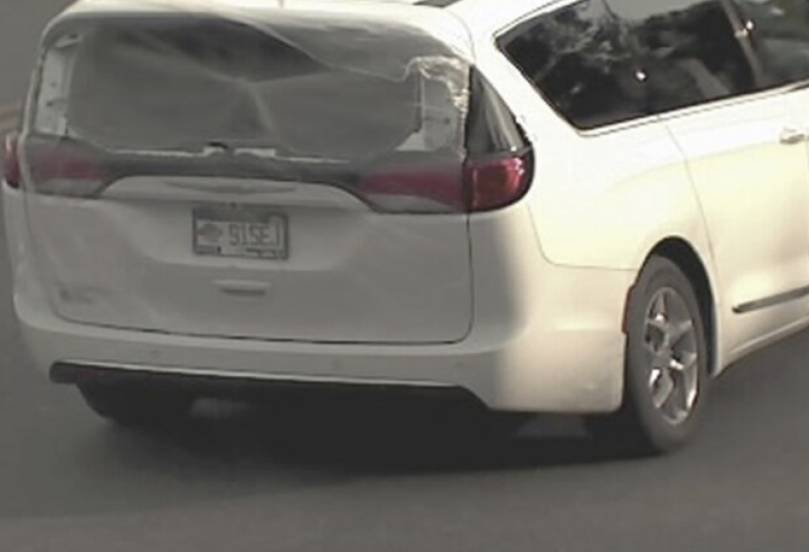 White minivan with its rear window covered in plastic, parked on an asphalt road.
