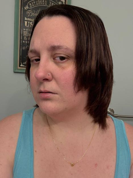 A woman with short, choppy hair and a sad expression looks at the camera.