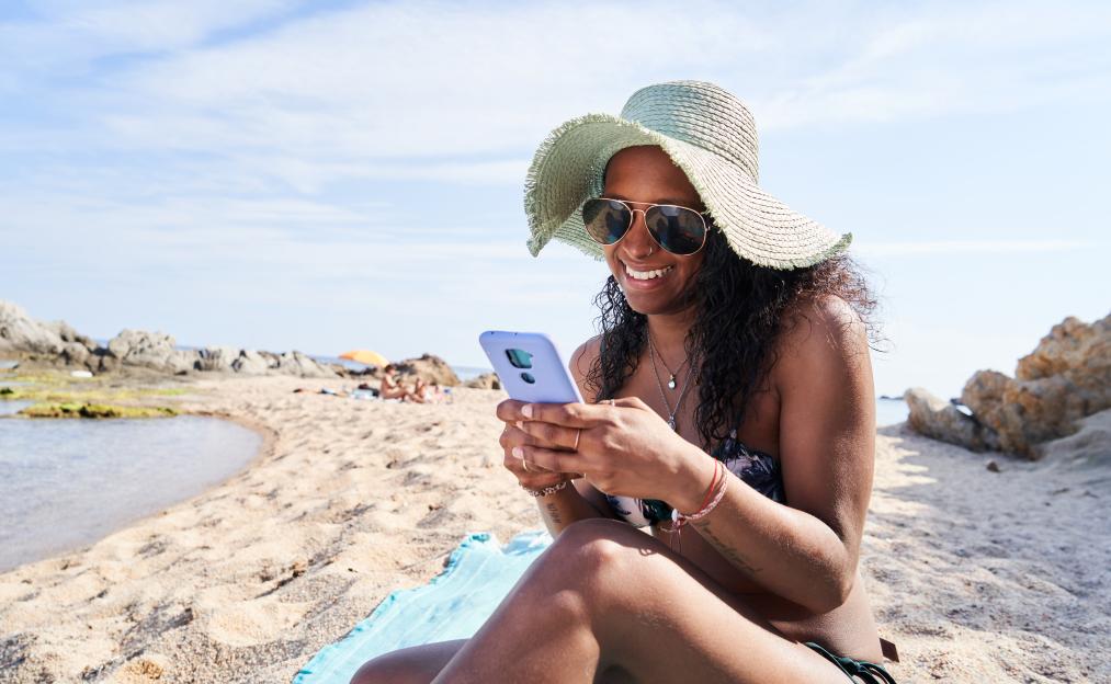 Cheerful young woman on the beach using a smartphone.