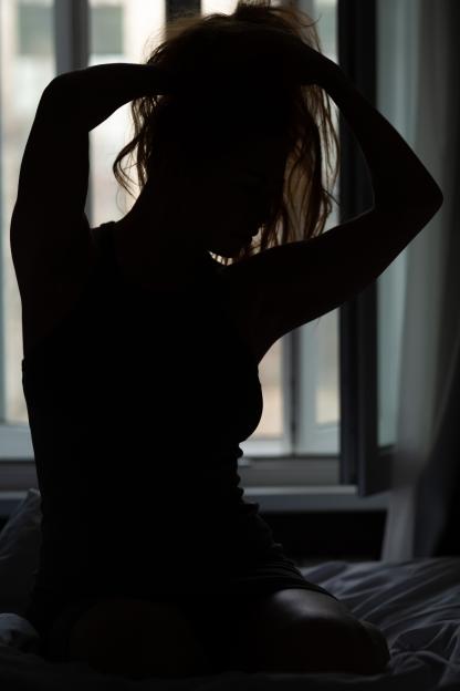 Silhouette of a beautiful slender woman sitting on a bed