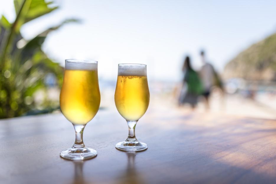 Two glasses of beer on a table at a beach bar.