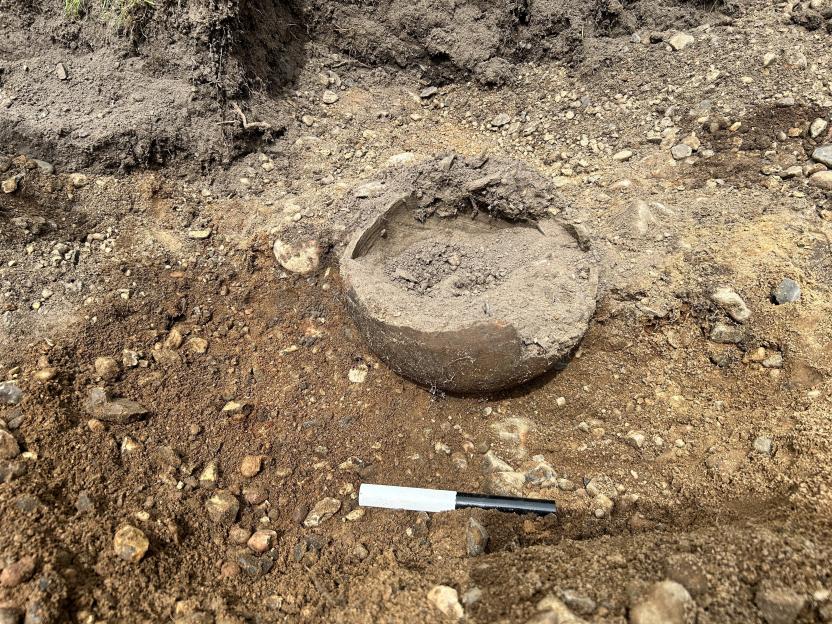 A ceramic vessel, partly buried in soil and rocks, contains hundreds of silver objects.