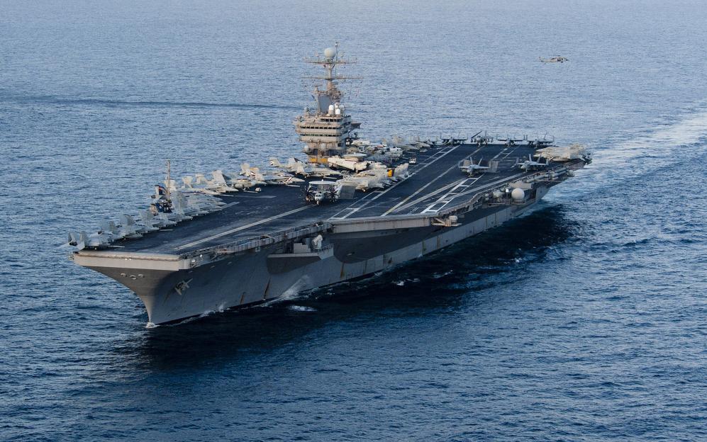 The Nimitz-class aircraft carrier USS Abraham Lincoln transiting the Arabian Sea with multiple aircraft on its deck, and a helicopter flying nearby.
