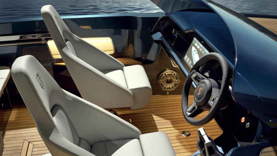 The interior of a sleek boat with light gray seats, a wooden floor, and a steering wheel with a Porsche emblem.