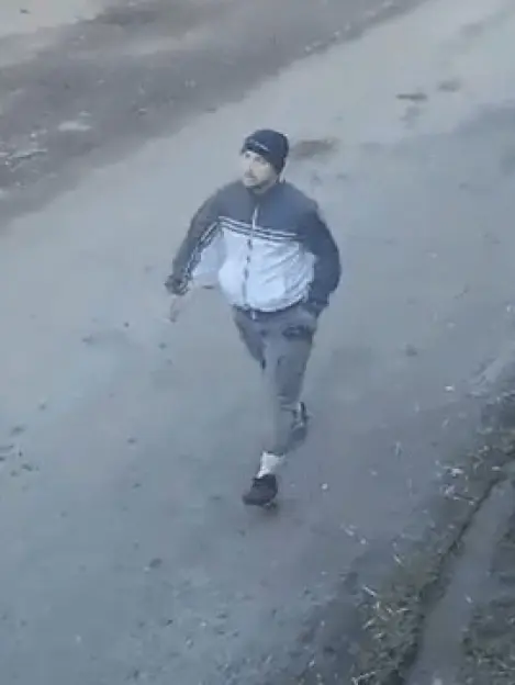 CCTV image of a man in a dark beanie and two-tone jacket walking on a dirt path.