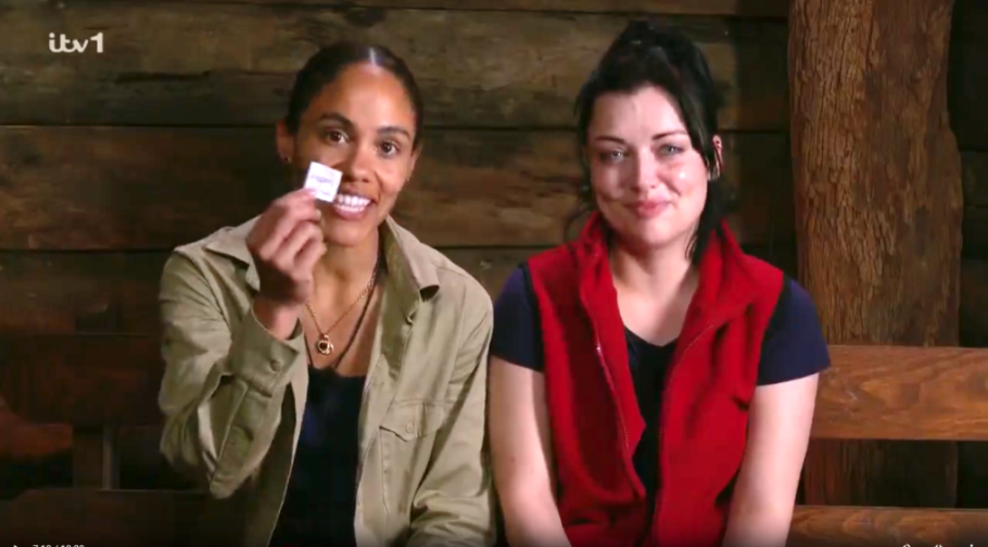 Two women on a television show, one holding a small white card.