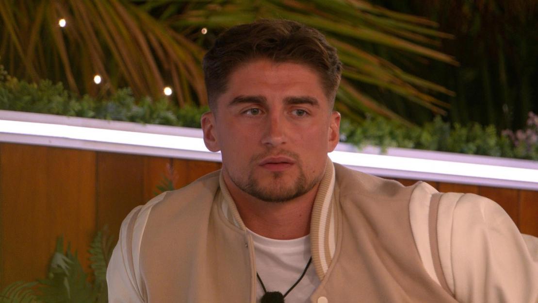 Man in a beige varsity jacket on "Love Island All Stars."