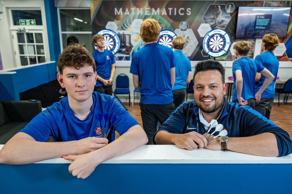 Jenson, a student, and Dave Wright, a geography teacher, pose with darts in front of a school darts team.